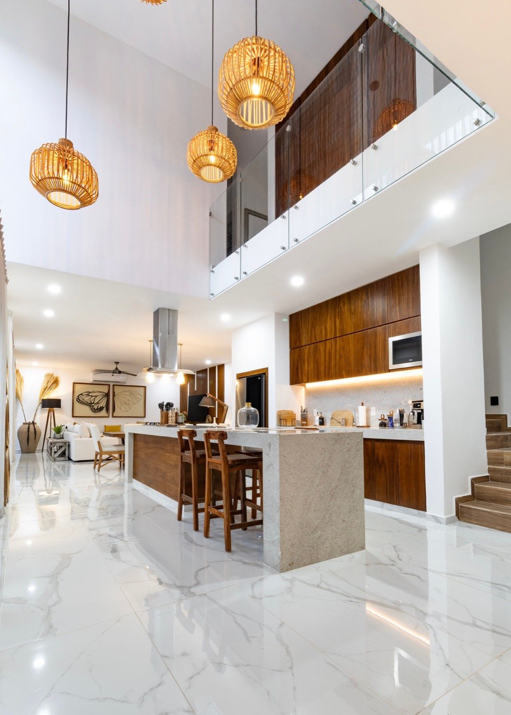 Bright open-plan kitchen and living space with a marble floor, timber cabinetry and a double-height ceiling.
